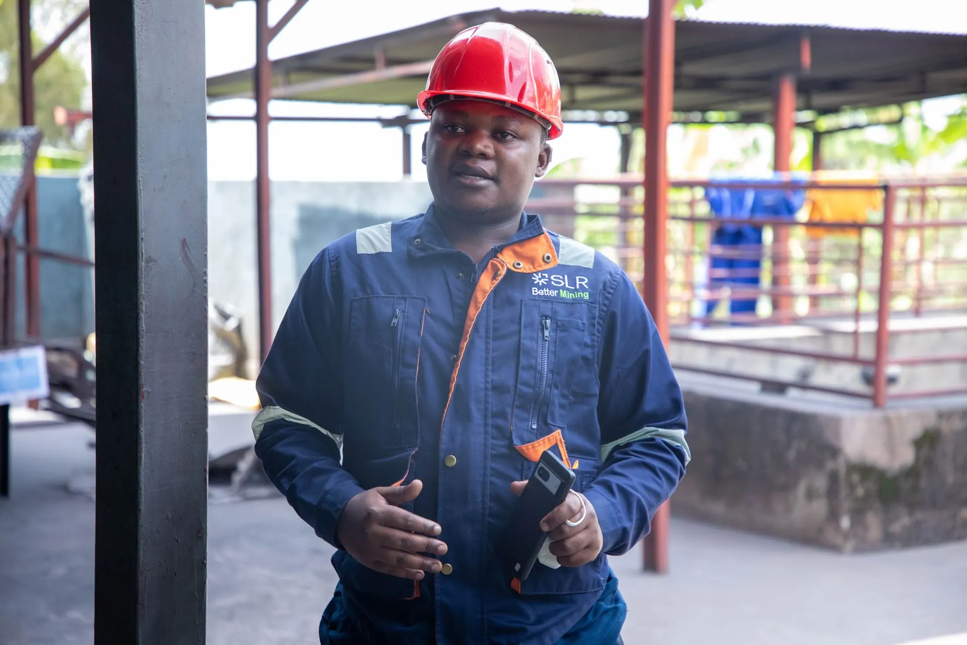 An engineer in navy coveralls and a red hard hat on site