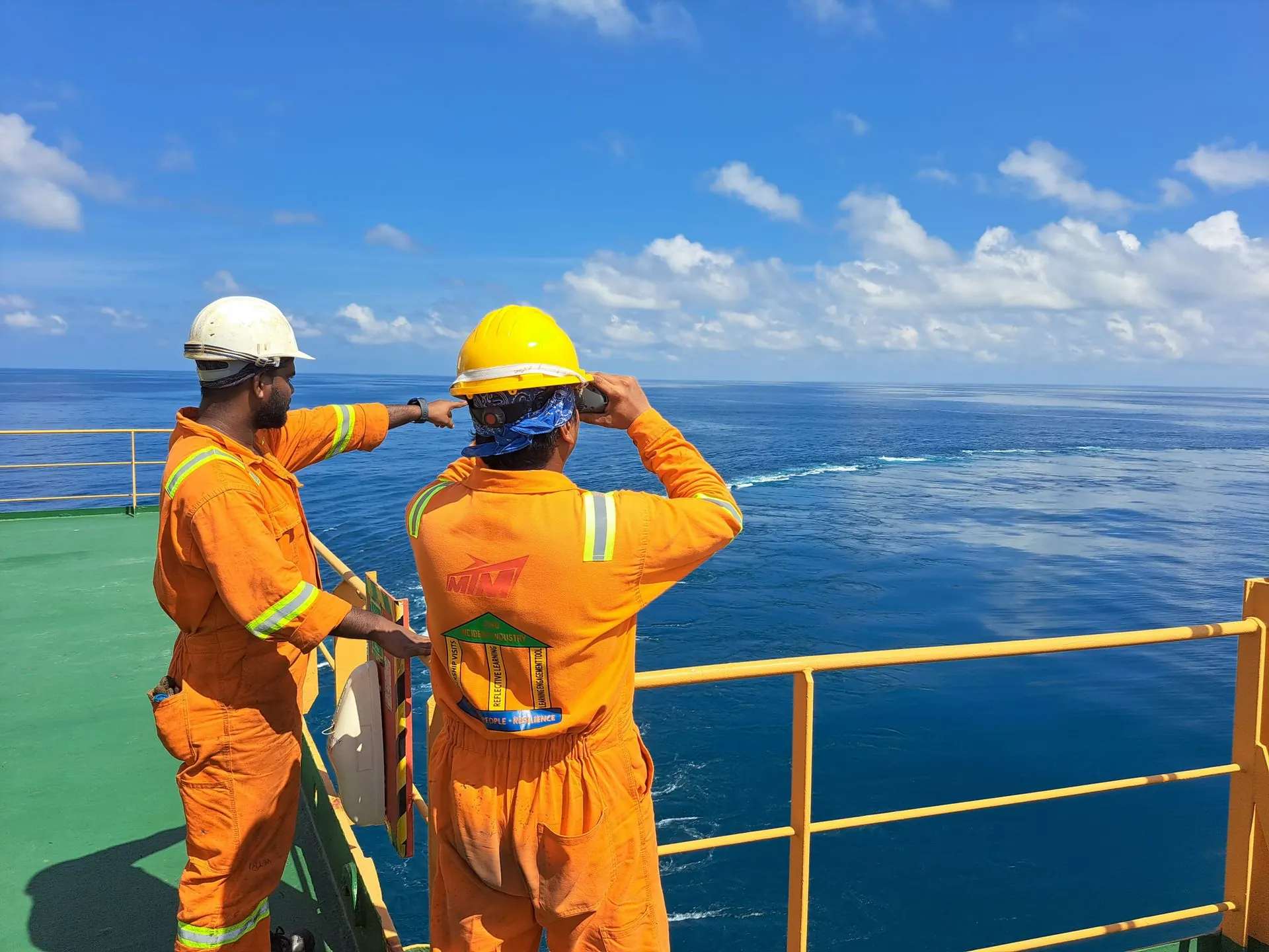 Two crew members in orange coveralls and hard hats on a vessel deck