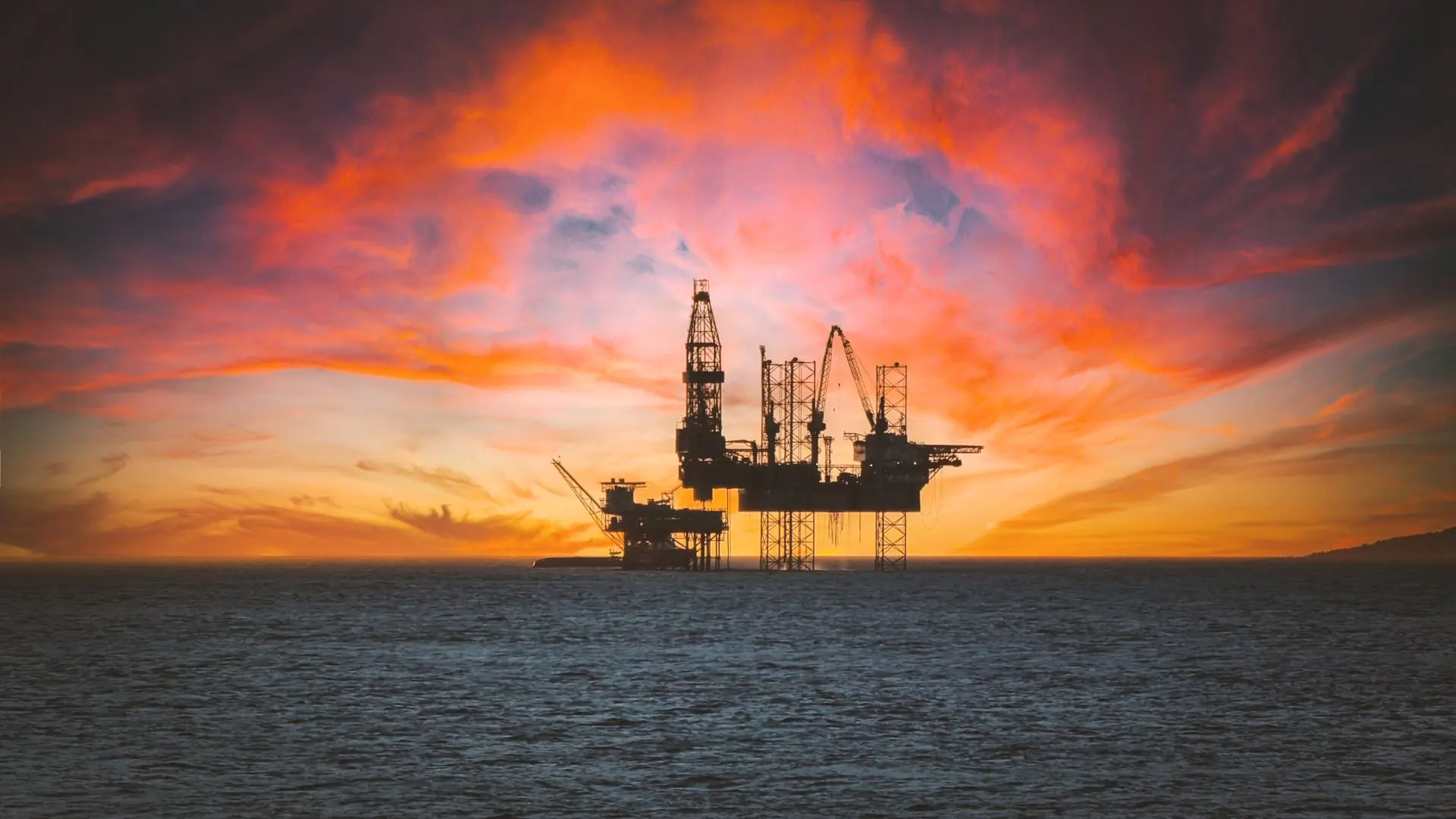 An offshore rig silhouetted against a red sunset